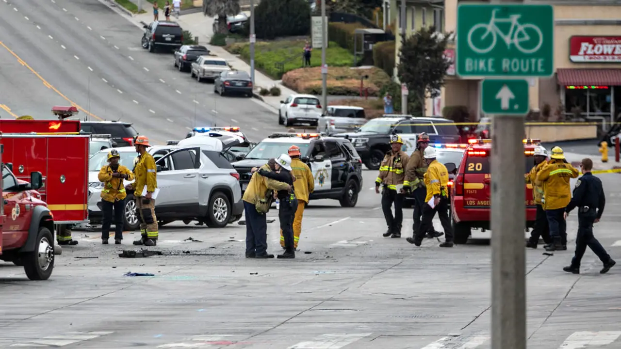 Emergency responders and firefighters attend to a multiple-vehicle accident on a city street with damaged cars and emergency vehicles present.